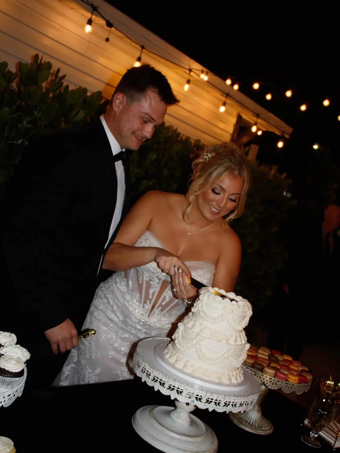Bride and groom cutting the wedding cake under string lights